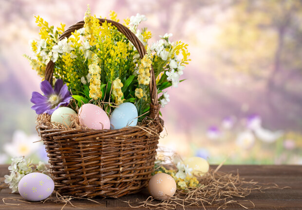 Ostereier und Blumen in einem Korb mit frühlingshaftem Hintergrund